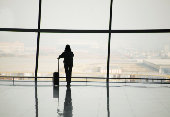 Silhouette of a woman with a suitcase at a large airport window