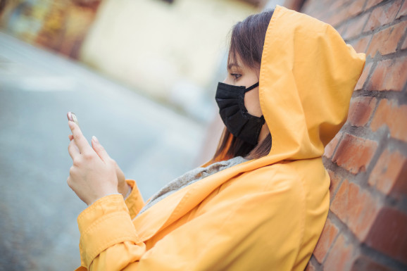 A young woman stares at her phone while wearing a face mask in a polluted city