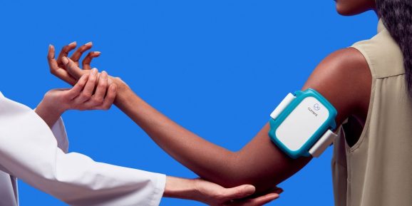 One person adjusts the arm position of a second person wearing a Current Health health-monitoring armband