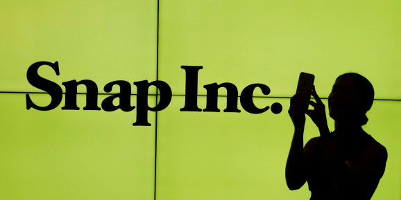 A woman stands in front of the logo of Snap Inc. on the floor of the New York Stock Exchange (NYSE) while waiting for Snap Inc. to post their IPO, in New York City