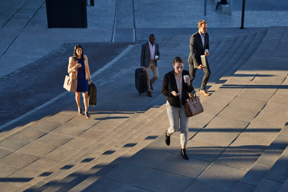 Businesspeople walking with bags on staircase outside, at sunrise