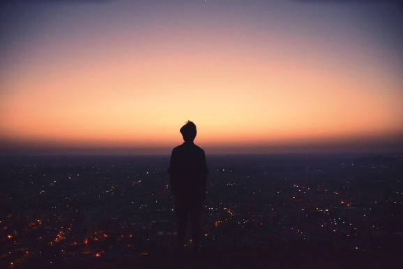 silhouette of a person on a hill top at dawn looking out over a city