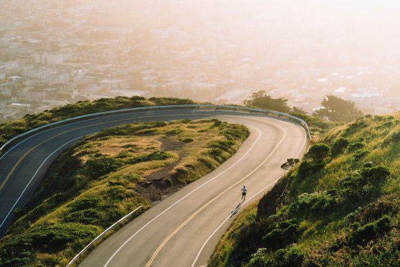 Aerial view of winding road on mountain against cityscape during sunset