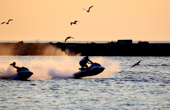Silhouette of jet ski riders heading out to ocean at dawn