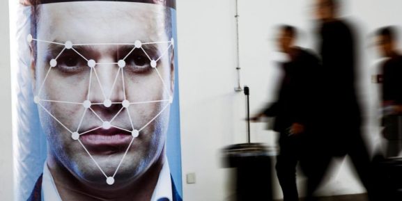 People walk past a poster simulating facial recognition software at the Security China 2018 exhibition on public safety and security in Beijing, China October 24, 2018.