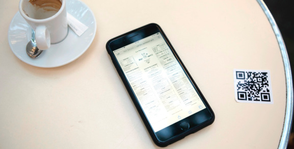 PARIS, FRANCE - JUNE 02: A phone with the menu is seen next to the qr code in order for customers to download the menu as the terrace is being set up at Les Marronniers Cafe