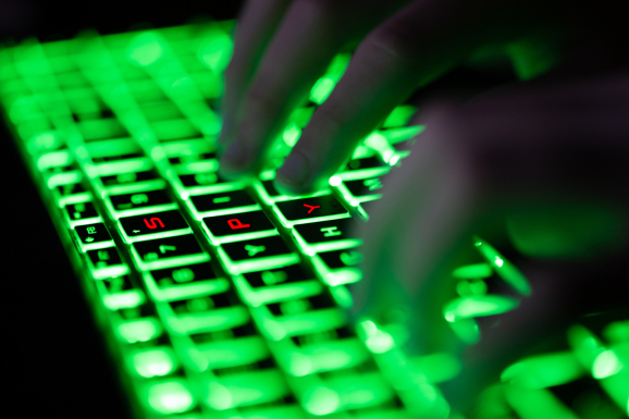 Digital composite of glowing green keyboard in the dark, the hands of a computer hacker typing and letters "SPY" in red on the keyboard