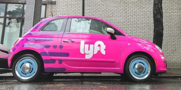 Fiat 500 painted pink and carrying a Lyft logo is parked in the streets of Manhattan.
