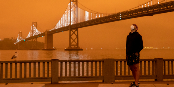 Eli Harik of San Francisco wears a mask while looking up at the dark orange sky hanging over the Embarcadero in downtown San Francisco, Calif. Wednesday, September 9, 2020 due to multiple wildfires burning across California and Oregon.